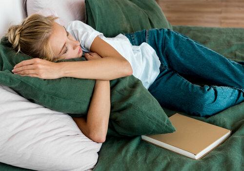 Atelier apnée du sommeil Une femme dort sur un lit, enlaçant un oreiller vert. Un livre fermé est posé à côté d'elle