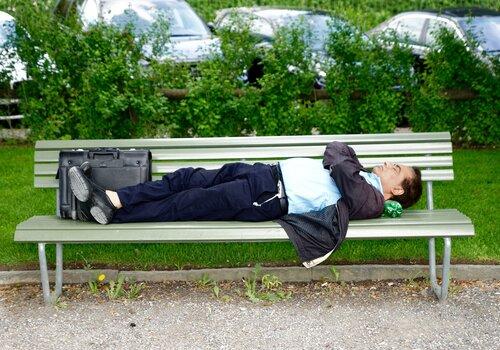 Dans un parc, un homme est allongé sur un banc, sa valise à ses pieds