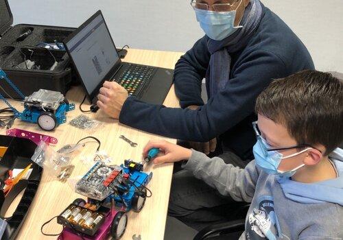 Un jeune accompagné par son père est en train de programmer un robot à l'aide du jeu vidéo Scratch
