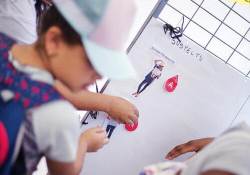 Enfants participants à une activité organisée par les étudiants de la faculté de sciences et technologies enfants face à un tableau d'enquête