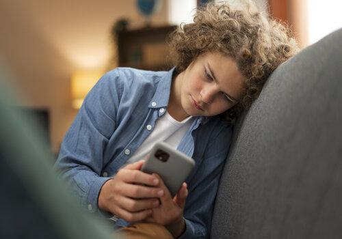 L'échappatoire Internet Jeune garçon a l'aire triste assis sur un canapé et regradant son téléphone