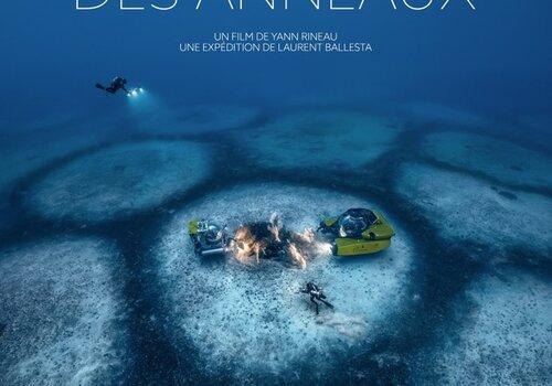 Deux petits sous-marins et des plongeurs au milieu d'un grand cercle jouxtant d'autres cercles dans la mer.