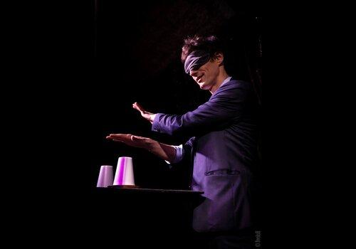 Visuel du spectacle de mentalisme présentant un homme avec les yeux bandés qui fait un tour les mains au-dessus de gobelets.