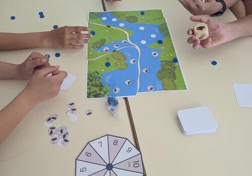 Les gardiennes des cours d'eau (jeu) Enfants autour d'un plateau de jeu représentant une rivière et des jetons de jeu.