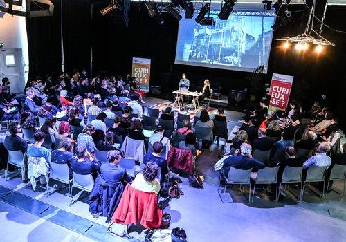 Défis environnementaux : Construire demain Texte alternatif concis : > Conférence avec deux intervenants sur scène face à un public nombreux, dans une salle sombre avec projection d’images.