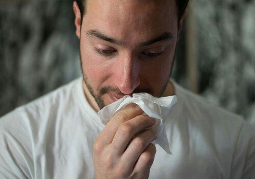 Un homme se mouche avec un mouchoir en papier.