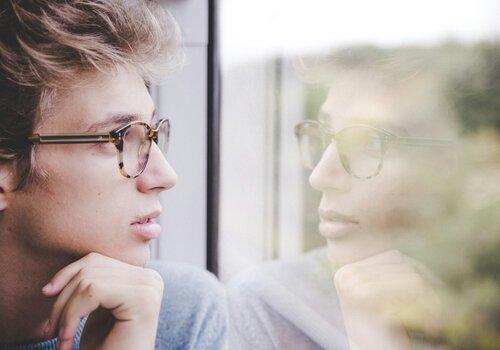Un homme avec des lunettes regarde à travers une fenêtre