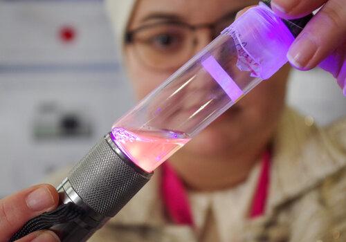 Une chercheuse montre un tube contenant un liquide luminescent