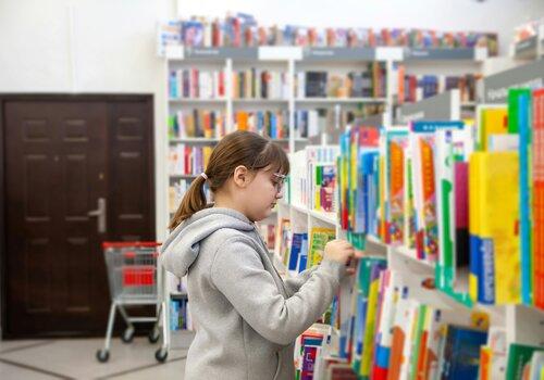Une petite fille cherche un livre dans un rayonnage de bibliothèque