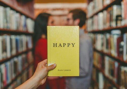 Personne tenant un livre avec une couverture jaune et le mot happy écrit dessus