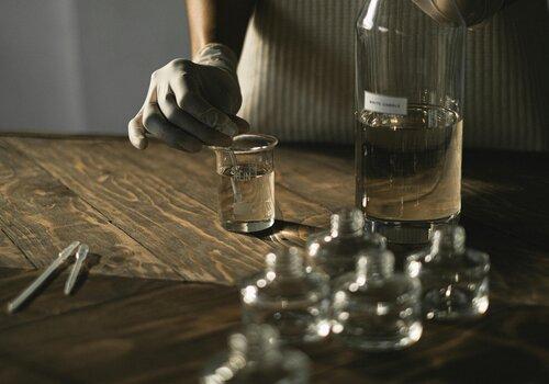 Une main gantée prélève un liquide contenu dans une fiole en verre