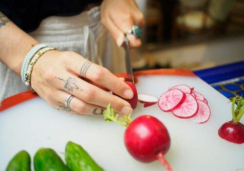 Une femme coupe un radis sur une planche en plastique blanc