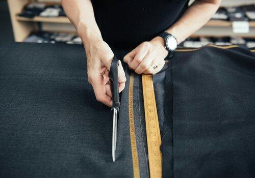 Une femme coupe du tissu noir à l'aide de ciseaux