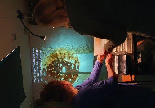 Matière terre agrandie et vue à travers de la lumière, avec une personne en transparence qui s'exclame les mains en l'air. 