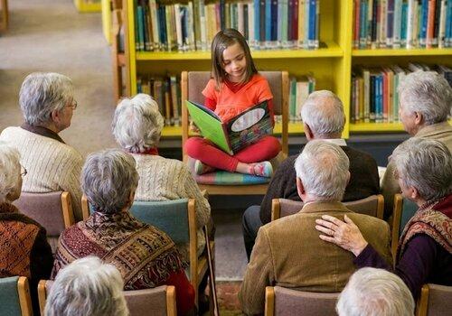 Une petite fille lit un album à un groupe de personnes aux cheveux blancs
