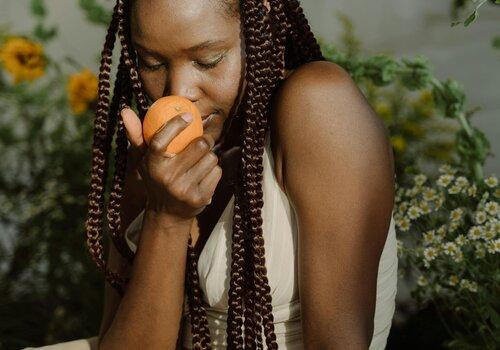 Une jeune fille sent une orange qu'elle tient dans ses mains.