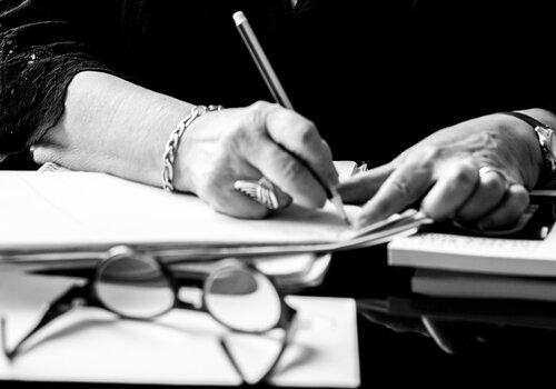 Image en noir et blanc d'une personne en train d'écrire, vue sur ses mains et sur son bureau