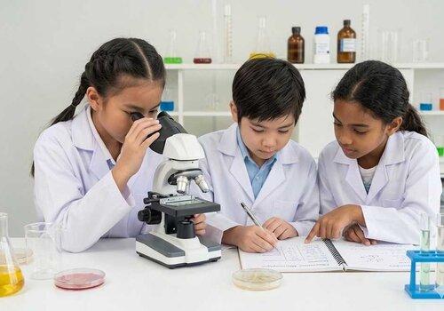 3 enfants en blouse de laboratoire, derrière un microscope