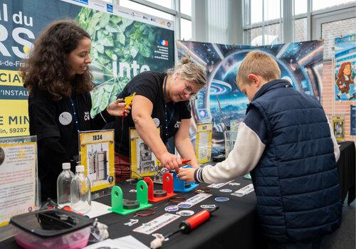 Deux scientifiques aident un jeune visiteur à participer à une expérience sur leur stand.