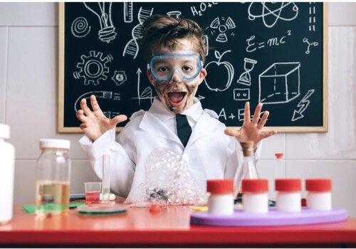 Un enfant abillé en blouse de laboratoire et lunette de protection est ébahi par les expériences qu'il réalise dans un mini-laboratoire