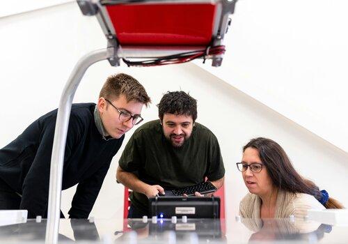 Deux hommes et une femme regardent un écran de programmation avec le sourire