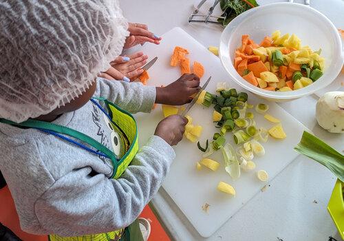 Un enfant épluche puis coupe des légumes