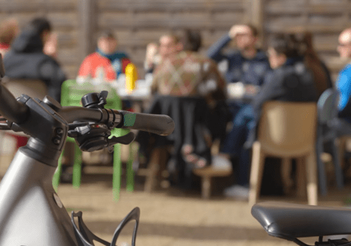 En premier plan, un guidon de vélo. En dernier plan, une tablée de personnes discutant
