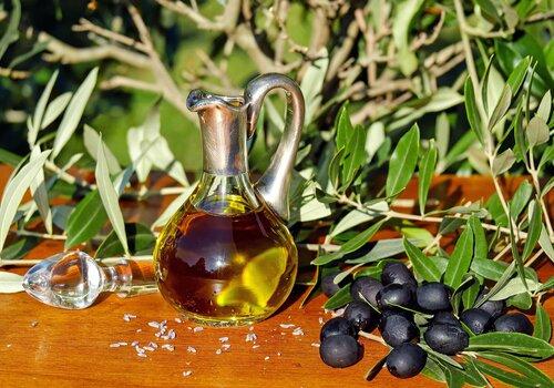 branches d'olivier en arrière plan avec au premier plan des olives noires et de l'huile d'olive