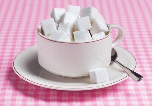 Sur une nappe vichy rose et blanc, une tasse à café blanche remplie de morceaux de sucre blanc.