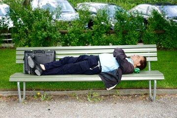 Dans un parc, un homme est allongé sur un banc, sa valise à ses pieds