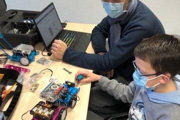 Un jeune accompagné par son père est en train de programmer un robot à l'aide du jeu vidéo Scratch