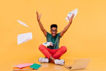 Les suprises de la science! Etudiant joyeux levant les bras, entouré de papiers, ordinateur...