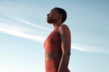 Femme noire en tenue de sport, en train de respirer profondément avec en arrière plan, un ciel bleu