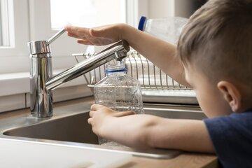 Enfant remplissant une bouteille en plastique au robinet