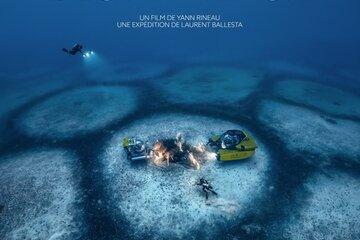 Deux petits sous-marins et des plongeurs au milieu d'un grand cercle jouxtant d'autres cercles dans la mer.