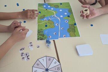 Enfants autour d'un plateau de jeu représentant une rivière et des jetons de jeu. 