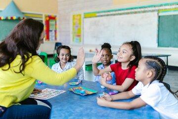 Des enfants en classe avec une enseignante. Une enfant 'high five' l'enseignante.