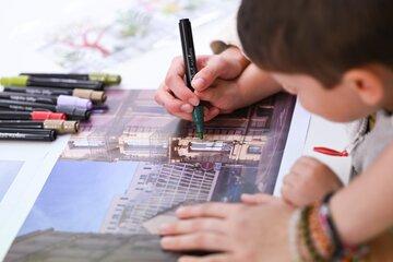 Texte alternatif concis :  > Enfant coloriant une photo de bâtiment avec des feutres, guidé par une main adulte.