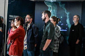 Des personnes attentives regardent une exposition interactive dans un espace sombre, avec une carte lumineuse en arrière-plan.