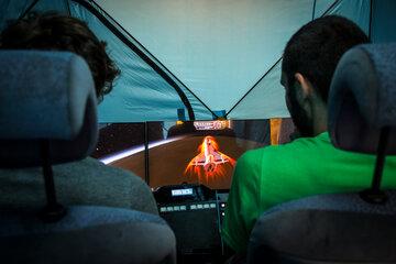 Deux hommes sont assis, de dos, aux commandes d'un écran qui représente une fusée en vol.