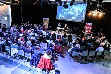 Défis environnementaux : Construire demain Texte alternatif concis : > Conférence avec deux intervenants sur scène face à un public nombreux, dans une salle sombre avec projection d’images.