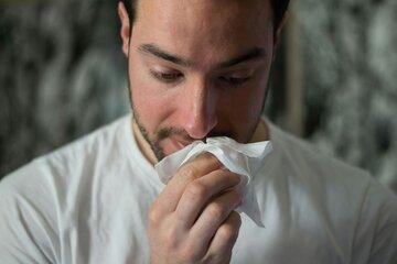 Un homme se mouche avec un mouchoir en papier.