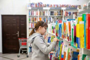 Une petite fille cherche un livre dans un rayonnage de bibliothèque