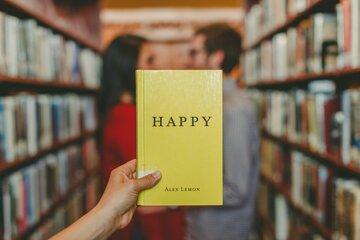 Personne tenant un livre avec une couverture jaune et le mot happy écrit dessus