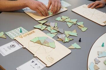 Plateaux, cartes, pions et pièces de jeux vert et marron sur une table avec des mains qui jouent
