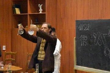 Un comédien interprète Louis Pasteur sur scène avec des ballons de chimie en verre dans les mains.