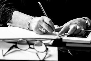 Image en noir et blanc d'une personne en train d'écrire, vue sur ses mains et sur son bureau