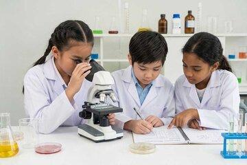 3 enfants en blouse de laboratoire, derrière un microscope