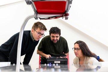 Deux hommes et une femme regardent un écran de programmation avec le sourire