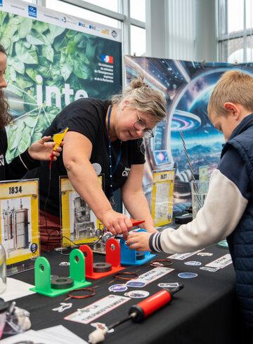 Deux scientifiques aident un jeune visiteur à participer à une expérience sur leur stand.